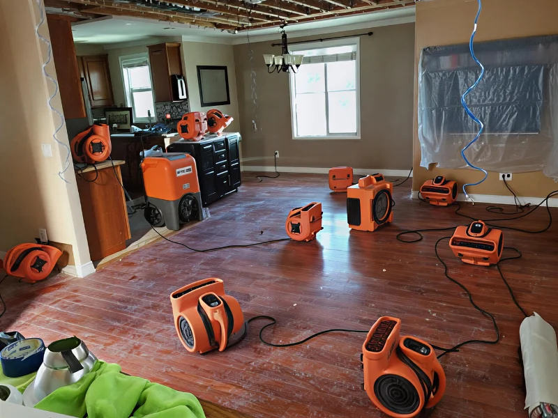 Multiple orange air movers and drying equipment spread across a hardwood floor in a room under renovation.