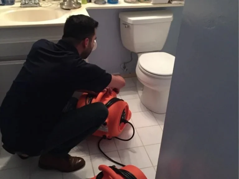 A man crouches in a bathroom adjusting an orange air blower near a toilet.