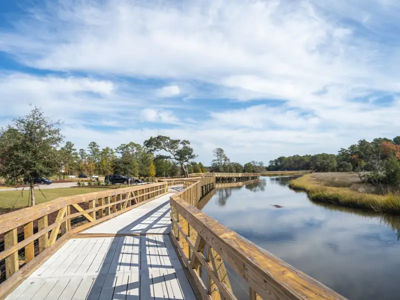 Wooden boardwalk curving alongside a calm river under a partly cloudy sky.