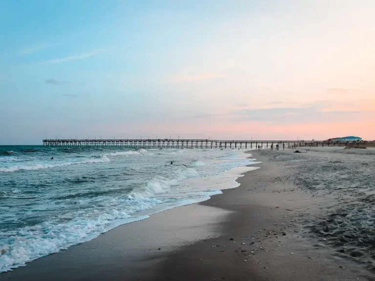 Ocean waves gently crashing on a sandy beach with a long wooden pier extending into the water.