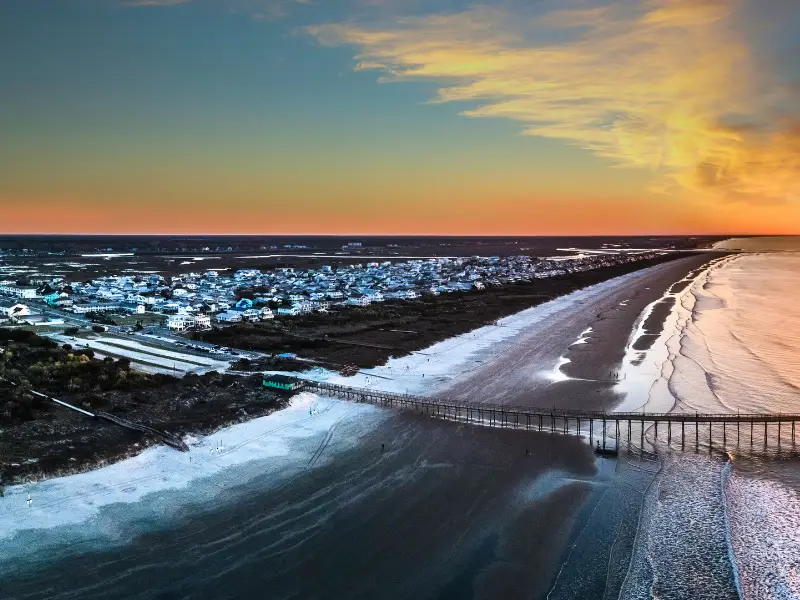 A coastal town with a long pier extending over the beach at sunset.