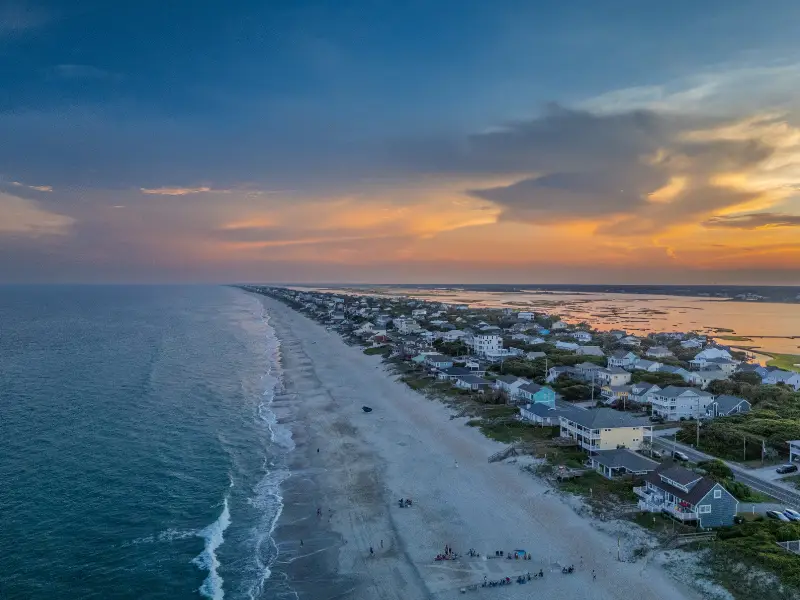 Aerial view of a coastal town with houses along a sandy beach at sunset.
