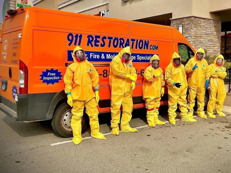 Six people in yellow hazmat suits and masks stand in front of an orange restoration service van.